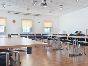 Un salón de conferencias con una larga mesa, varias sillas y proyectores instalados en el techo.