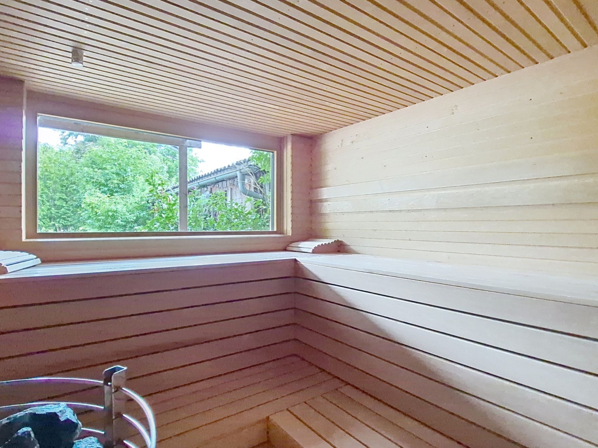 Un sauna con listones de madera, una ventana y vistas al follaje exterior.