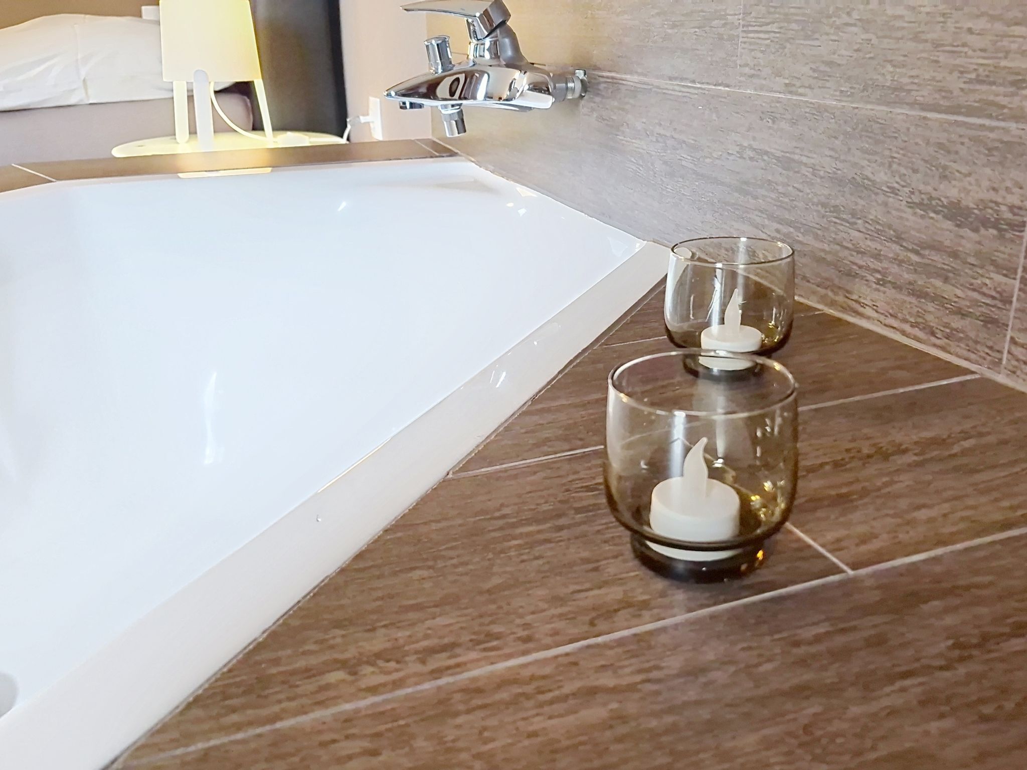 Ein Badezimmer mit einer weißen Badewanne, einem Glas-Kerzenhalter und einem modernen Wasserhahn.