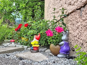 A garden with decorative statues, a potted plant with pink flowers, and a stone wall.