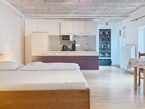 A modern bedroom with a wooden bed, a kitchenette with a microwave, and a dining area with a table and chairs. - Böhmerwald Pur2 by Interhome (Klaffer am Hochficht)