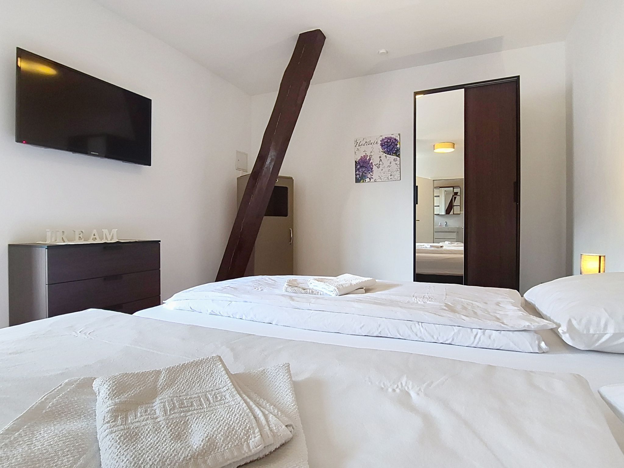 Una habitación de hotel con cama, cómoda, televisor y espejo.