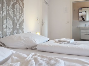 Een hotelkamer met een bed, kussens, een opgevouwen handdoek, een badkamer met een wastafel en een spiegel.