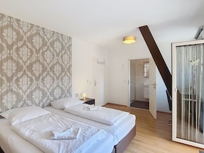 A hotel room with two beds, a nightstand, a lamp, a wardrobe, and a mirror.
