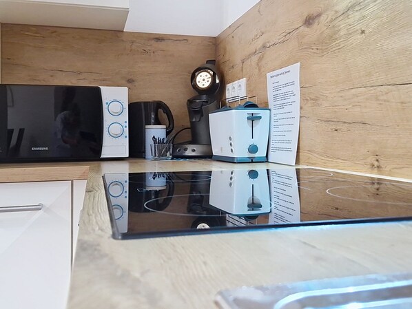 A kitchen with a microwave, coffee maker, toaster, and a clock on the wall.