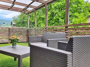 Een terras buiten met rieten meubels en een tafel, omringd door een houten schutting en groen.