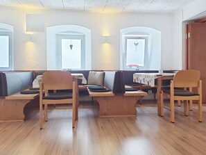 A seating area with wooden benches and chairs, a white wall with a window, and a ceiling with a textured finish.