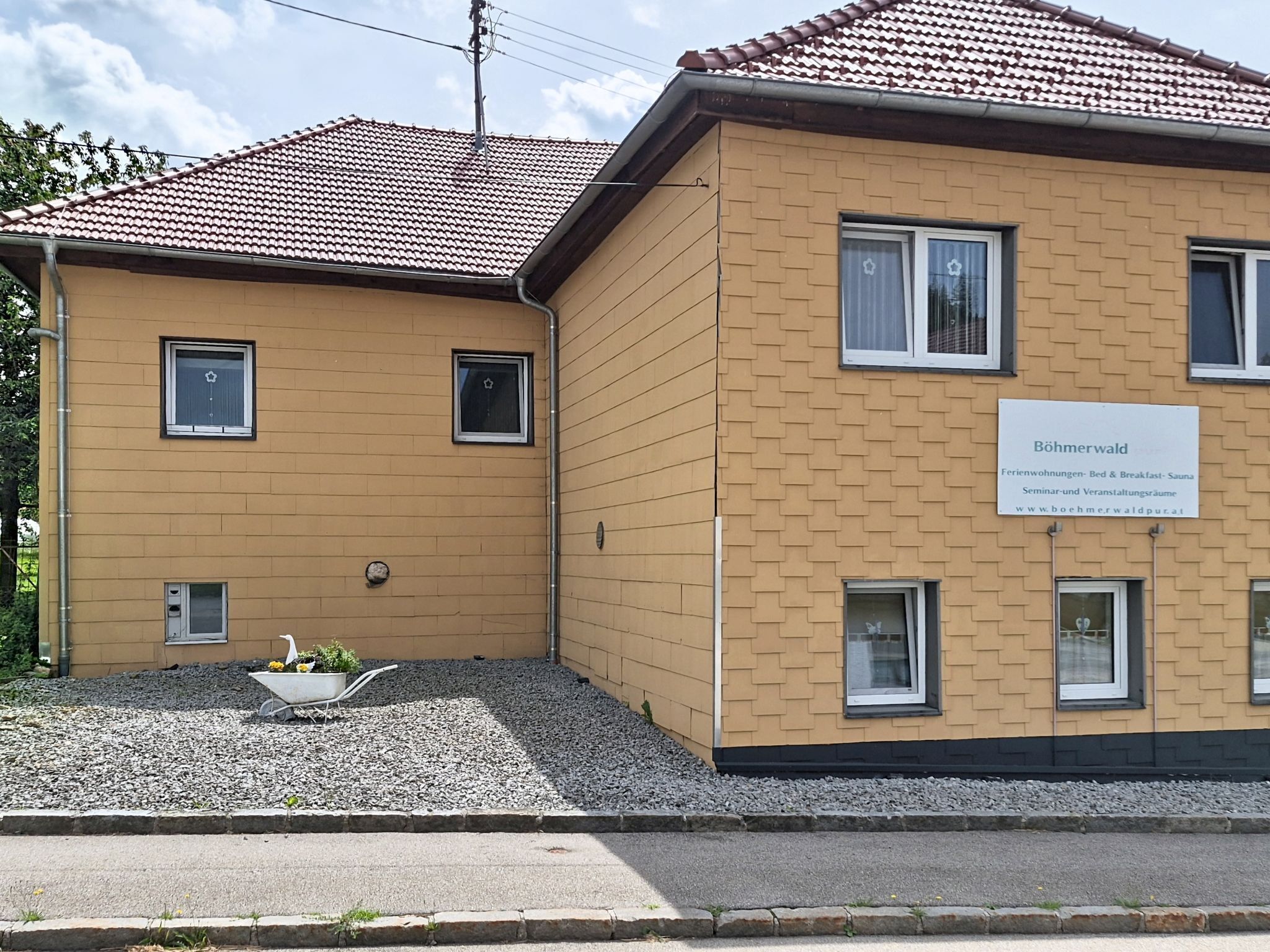 A two-story building with a sign indicating it is a guesthouse offering bed and breakfast, sauna, seminar rooms, and event space.
