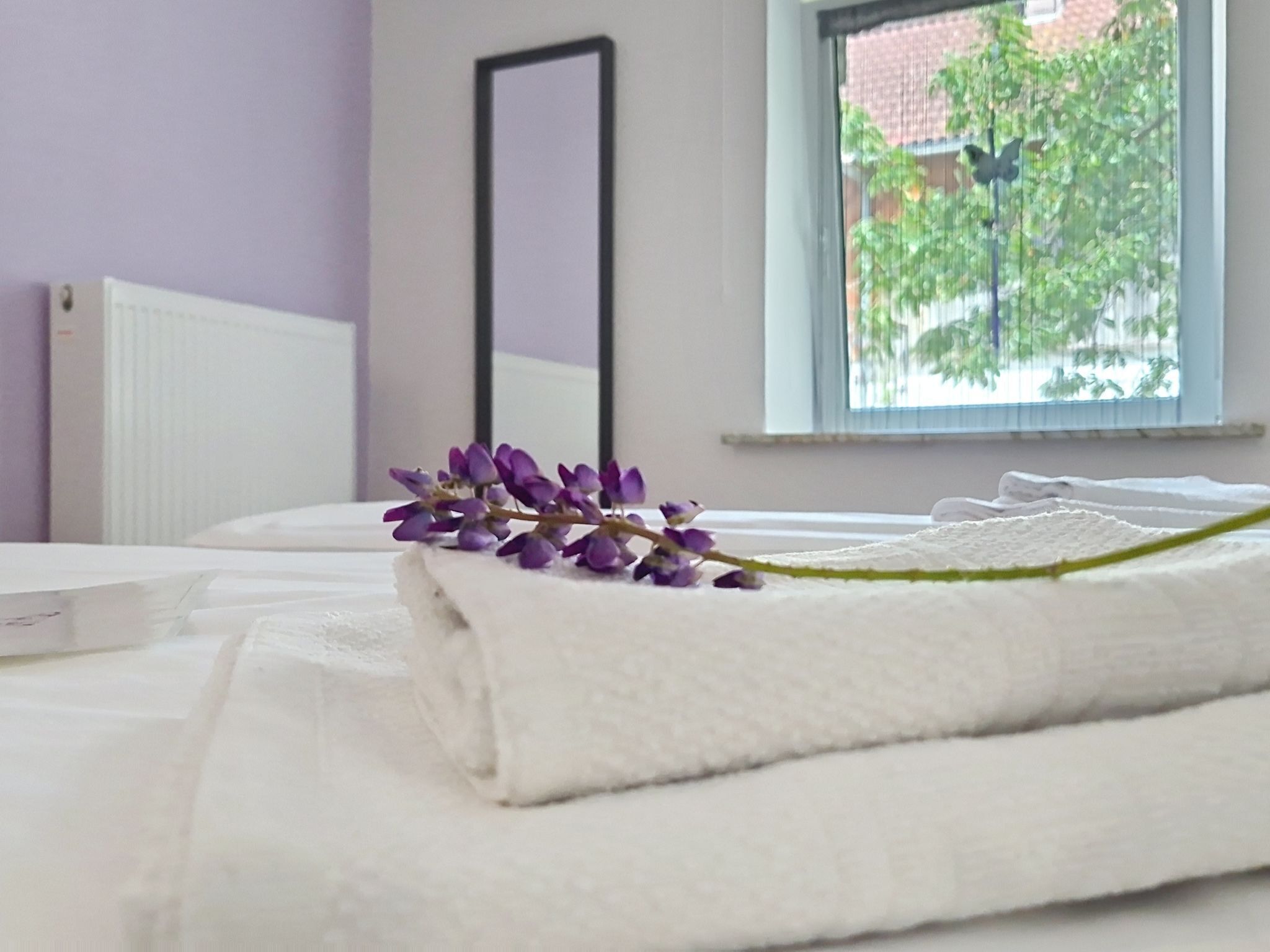 A neatly made bed with a white duvet and a purple flower decoration.