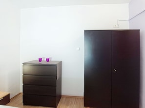 A room with a dark-colored wardrobe and a small dresser with two purple cups on top.