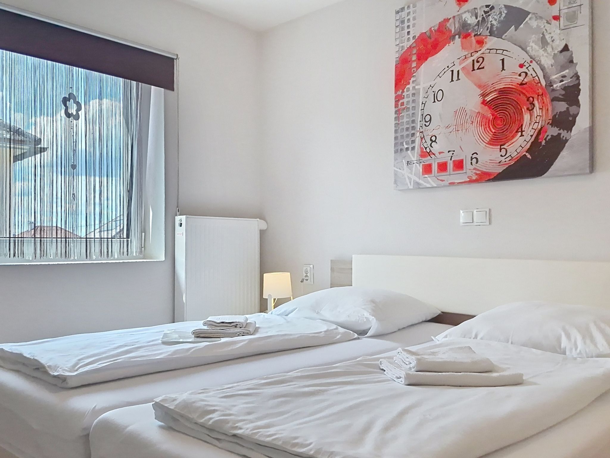 A hotel room with two beds, a large abstract painting on the wall, a window with blinds, and a radiator.