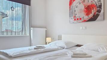 A hotel room with two beds, a large abstract painting on the wall, a window with blinds, and a radiator.