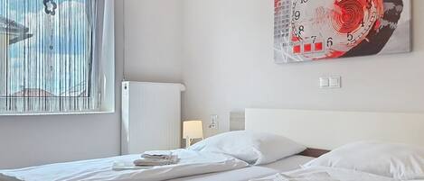 A hotel room with two beds, a large abstract painting on the wall, a window with blinds, and a radiator.