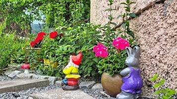 Een tuin met decoratieve beelden, een potplant met roze bloemen en een stenen muur.