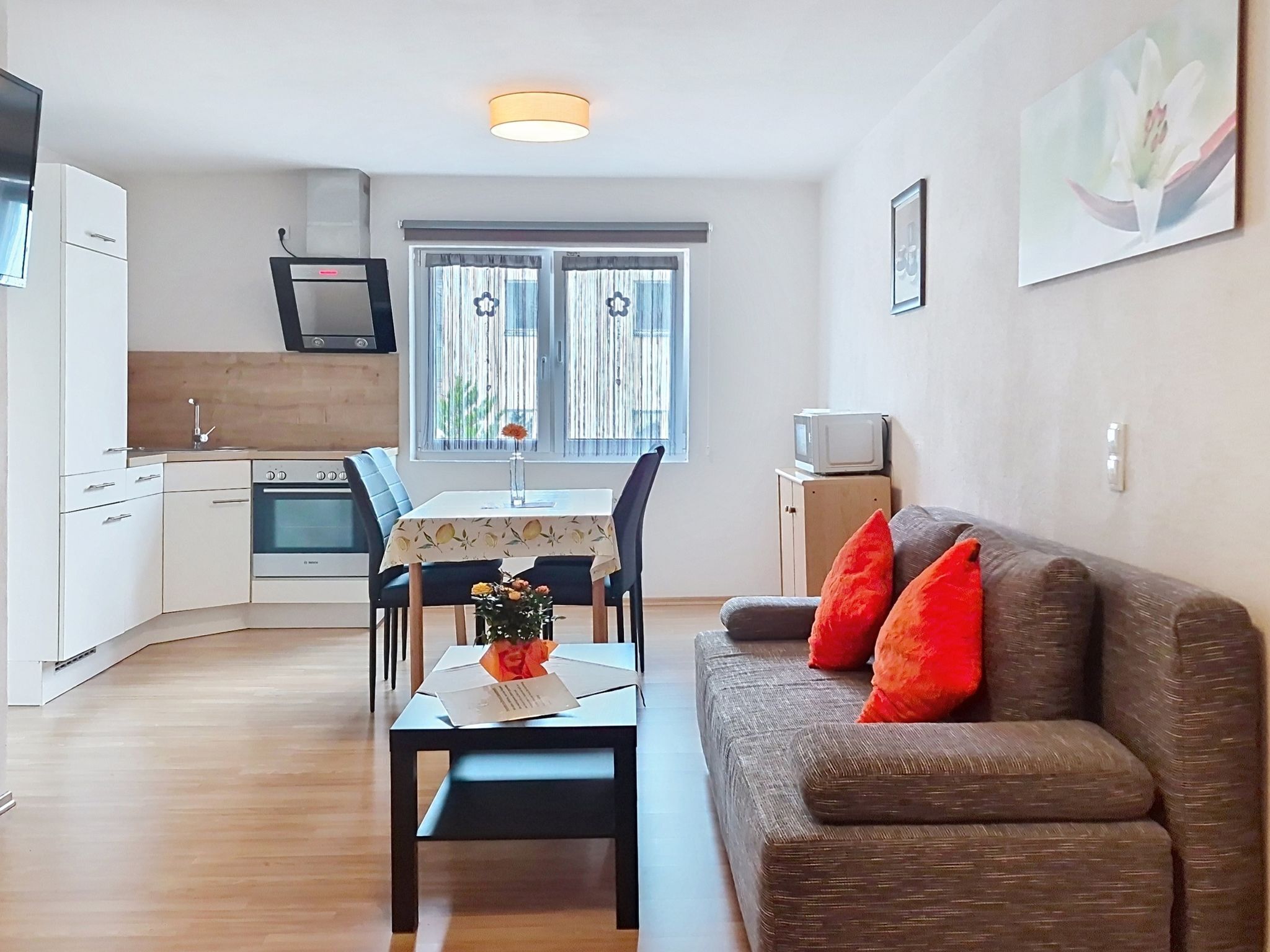Een ruimtelijk ingerichte leefruimte met een kitchenette, een eethoek en een bank met rode kussens.