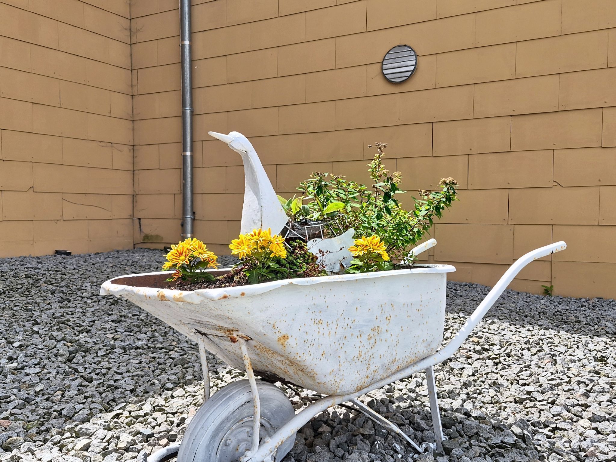 En trillebør med blomster og en dekorativ engelstatue foran en bygning.