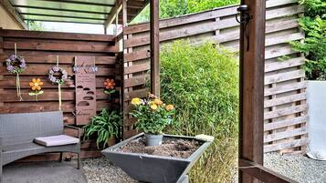 En overdækket patio med en træbænk, en plantekasse med blomster og en pergola over hovedet.