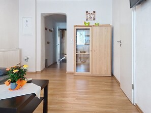 Une pièce avec un plancher en bois, une table ornée d’un vase de fleurs, un meuble avec des portes en verre et un radiateur.