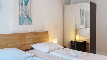 A hotel room with a wooden headboard, a bed with white linens, a nightstand with a lamp, and a large mirror reflecting the room.
