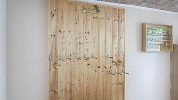 A wooden wardrobe with multiple doors and hooks, a small shelf unit with glass doors, and a ceiling with a speckled pattern.