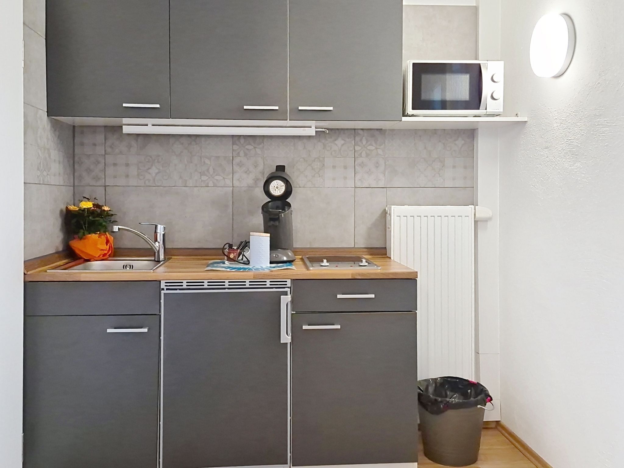 Una cocina compacta con gabinetes grises, un microondas, un fregadero y un pequeño bote de basura.