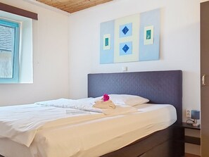 Habitació d'hotel amb un llit, una finestra amb persianes, una obra d'art penjada a la paret i una taula de nit amb una làmpada.