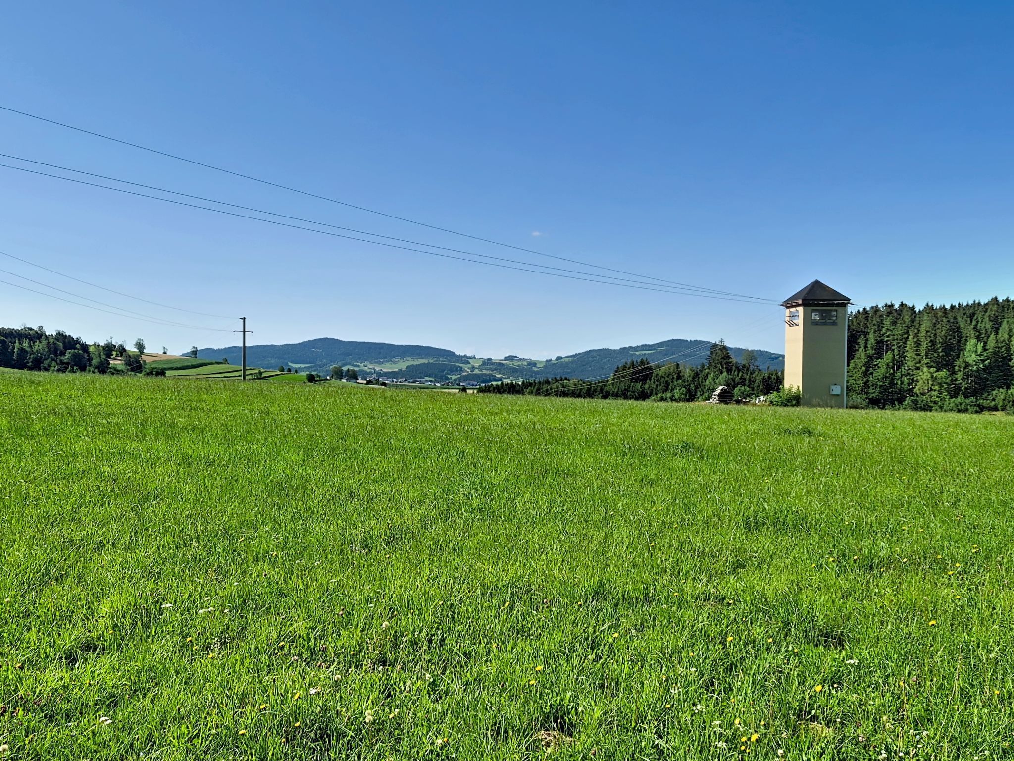 A rural landscape with a tower structure, open fields, and distant hills.