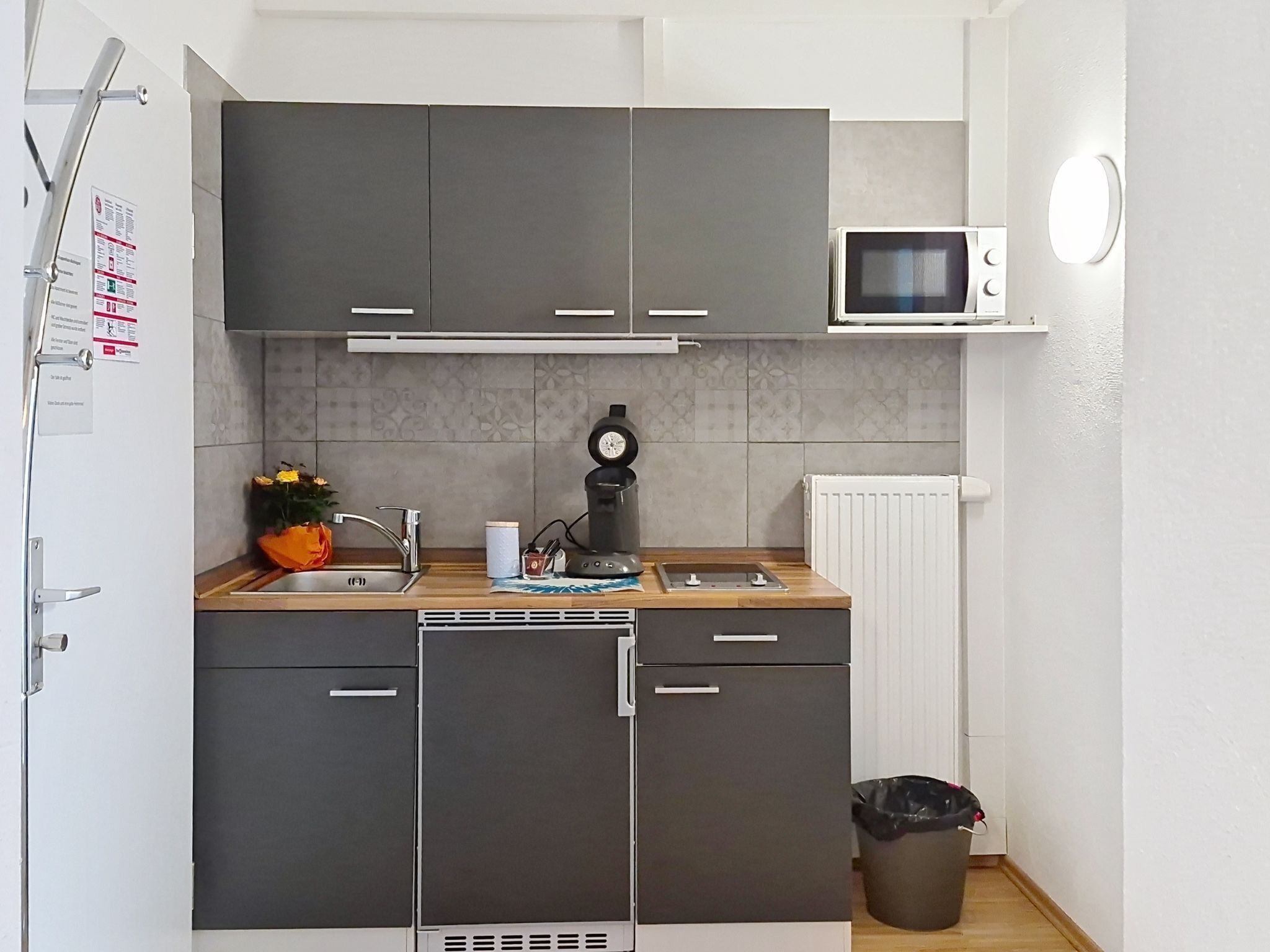 Una cocina compacta con armarios grises, un microondas, una cafetera y un pequeño cubo de basura.