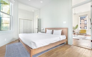 A modern bedroom with a wooden bed, white bedding, and a view of the outside through a large window. - Park House Carriage, Just Steps from Forsyth Park (Savannah)
