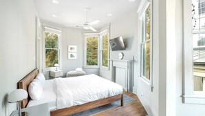 Un dormitorio con cama, mesita de noche, lámpara, televisor, chimenea y ventanas amplias.
