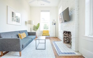 A living room with a grey sofa, a yellow chair, a coffee table, a fireplace, and a TV mounted on the wall. - Park House Carriage, Just Steps from Forsyth Park (Savannah)