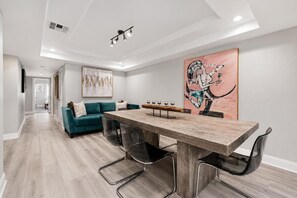 Un salon moderne avec un canapé de couleur turquoise, une table à manger en bois avec des chaises, et un grand tableau abstrait accroché au mur.