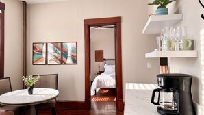 Una habitación de hotel con cama, una mesa de comedor con sillas, una cafetera y obras de arte en la pared.