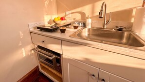 Una cocina con un lavamanos de acero inoxidable, una cafetera, un cuenco de fruta y un microondas.