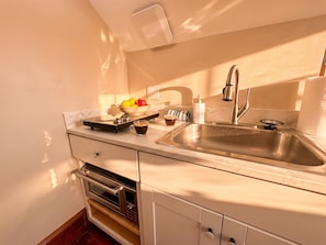 A kitchen with a stainless steel sink, a coffee maker, a bowl of fruit, and a microwave.