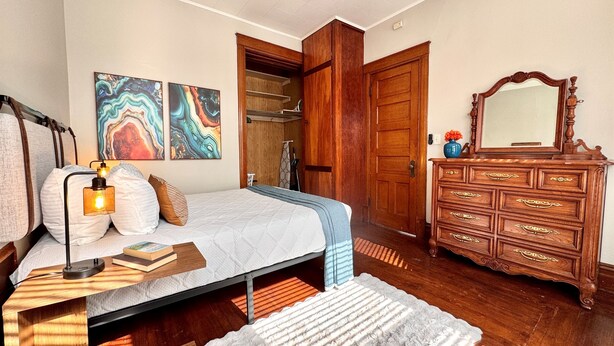 Un dormitorio con cama, mesita de noche, lámpara, cómoda, espejo, obra de arte y una puerta que da al baño.