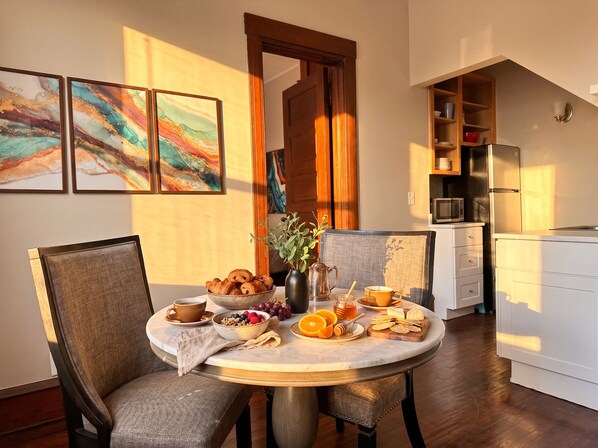 A dining area with a round table, chairs, a bowl of croissants, a vase with flowers, and a coffee cup.