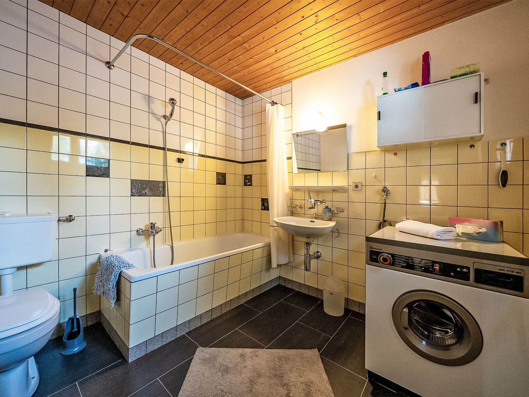 Een kleine badkamer met bad, toilet, wastafel en een wasmachine.
