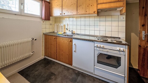 A compact kitchen with wooden cabinets, a built-in oven, and a window above the sink. - Chesa Quadrellas / EG by Interhome (Samedan)