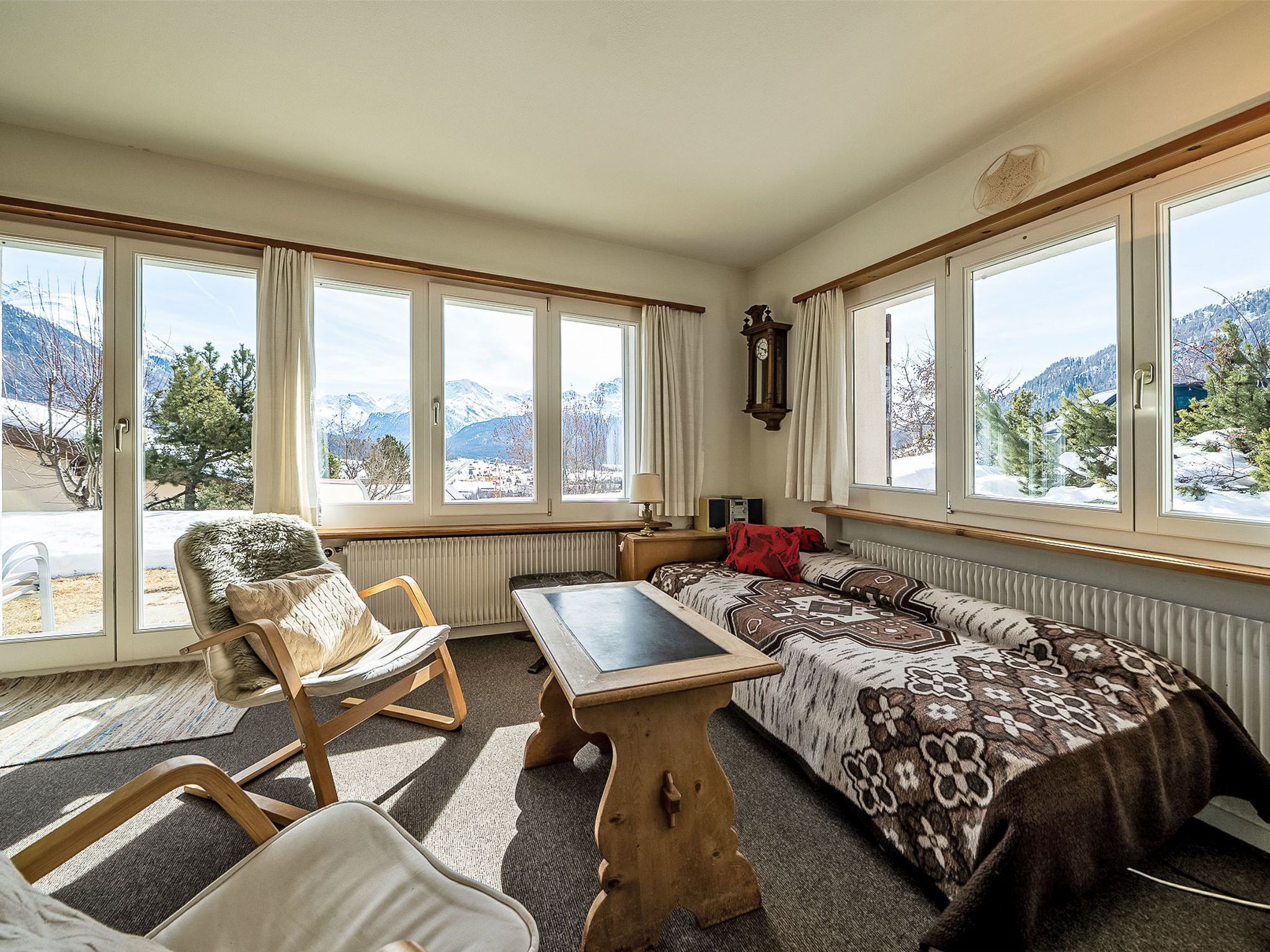 A room with large windows, a wooden table, a sofa, and a chair.