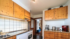A kitchen with wooden cabinets, a white stove, and a countertop with a kettle and toaster. - Chesa Quadrellas / EG by Interhome (Samedan)