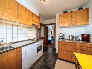 A kitchen with wooden cabinets, a white stove, and a countertop with a kettle and toaster. - Chesa Quadrellas / EG by Interhome (Samedan)