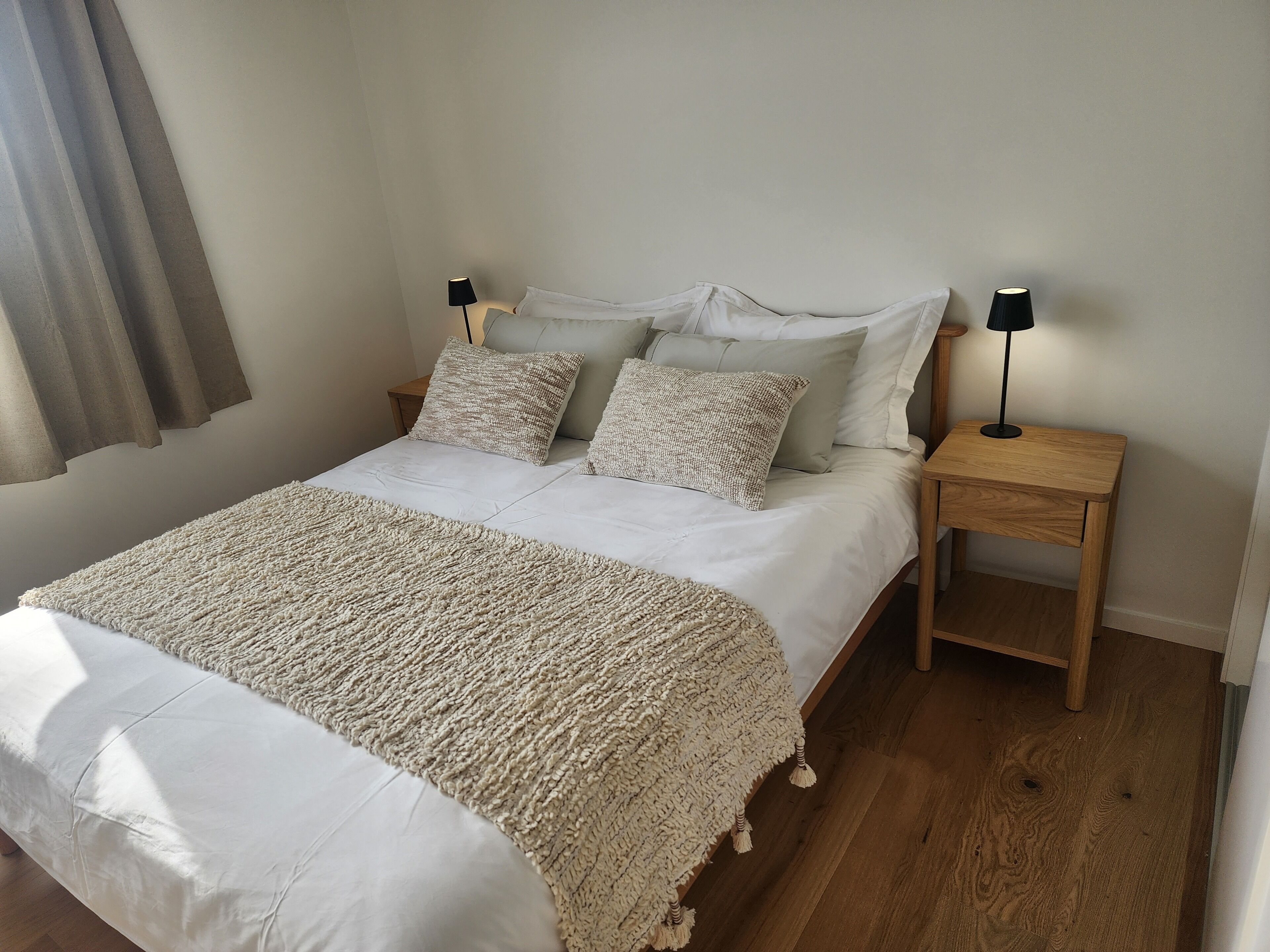 A neatly made bed with a textured blanket, two bedside lamps, and a wooden nightstand.
