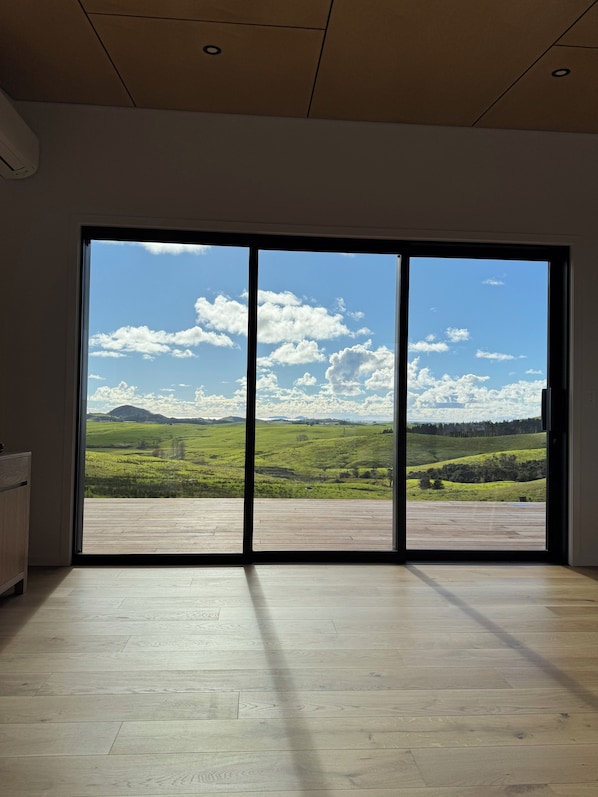 Une pièce dotée d’une grande porte-fenêtre coulissante donnant sur un paysage verdoyant et un ciel dégagé.