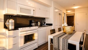 A modern kitchen with white cabinetry, a built-in microwave, and a dining area with a table and chairs.