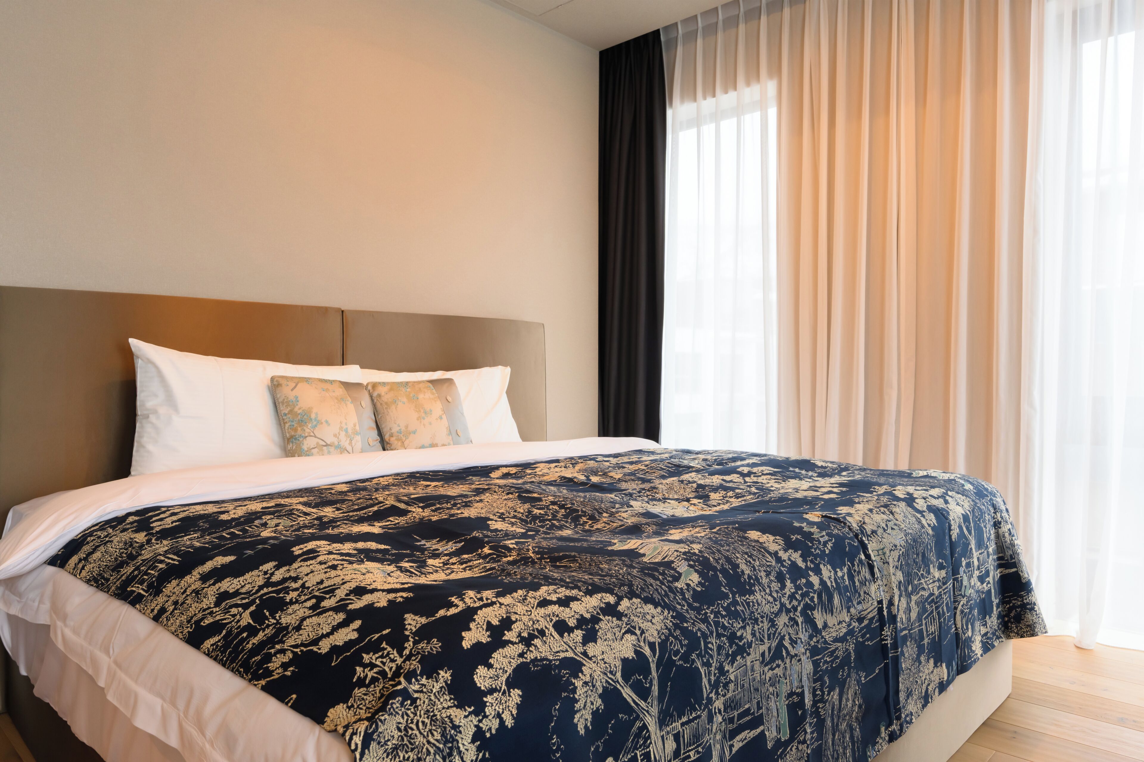 A hotel room with a large bed, a headboard, and a window with curtains.