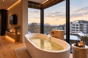 A modern bathroom with a freestanding bathtub, a wooden vanity, and a large window offering a city view.