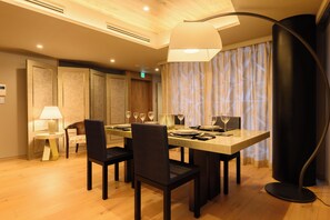 Ein Hotel-Essbereich mit einem großen Tisch für vier Personen, Stühlen, einer Stehlampe und einem Fenster mit Vorhängen.