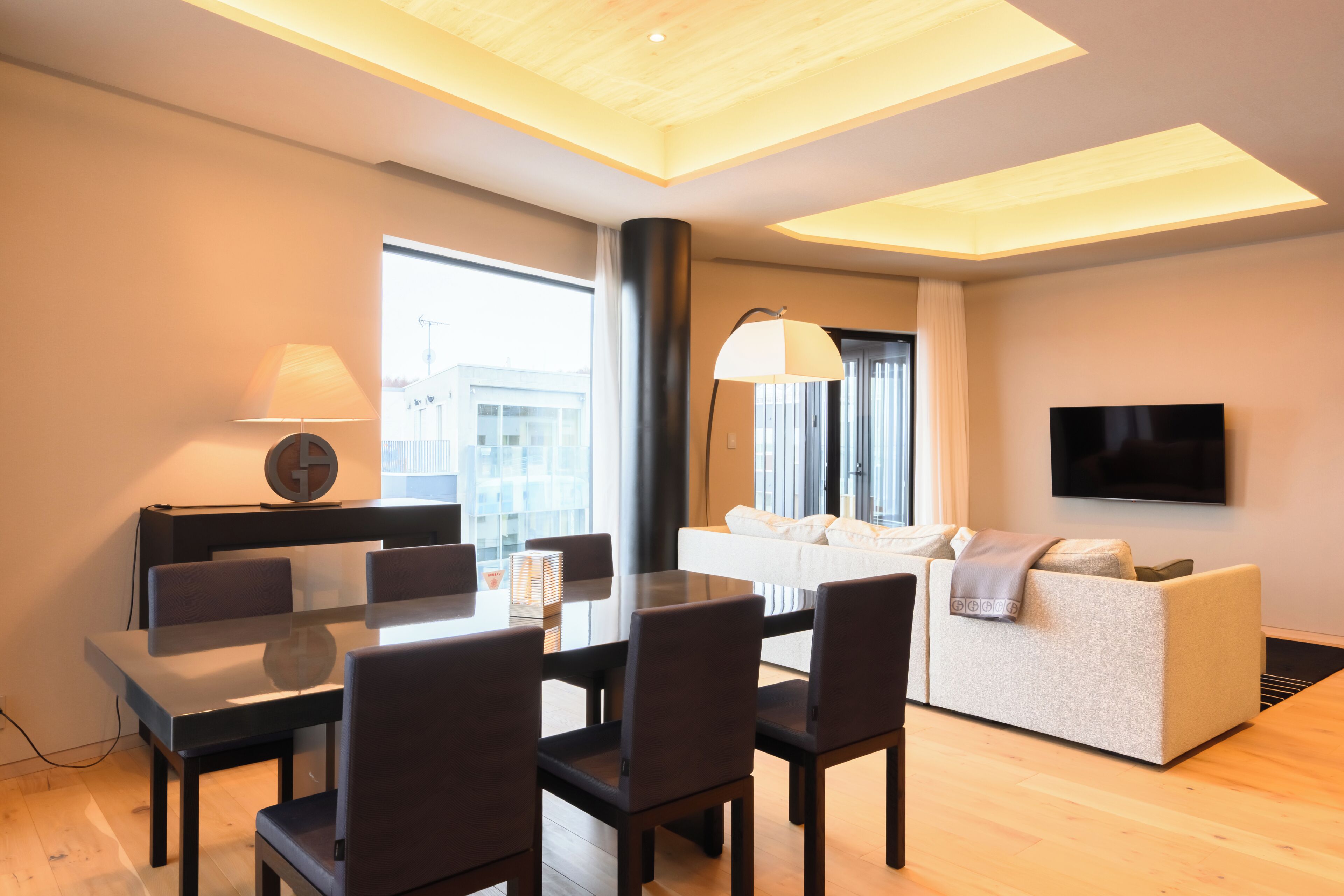 Una sala de estar moderna con comedor, un sofá, un televisor y un ventanal grande.