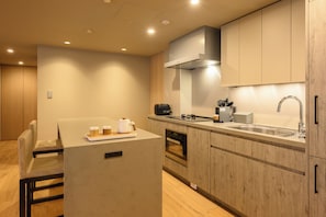 A compact kitchen with a built-in oven, a sink, and a stove. There is a dining area with a table and chairs. - HOTELA Niseko Towers  (Kutchan)